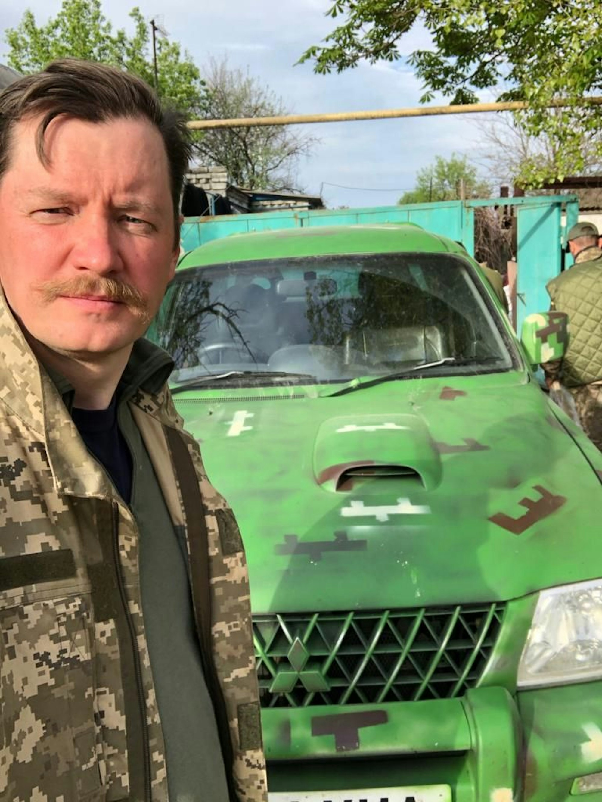 Mykola Hryhorenko steht im Flecktarn vor einem grünen Militärfahrzeug an der Front im Donbass.