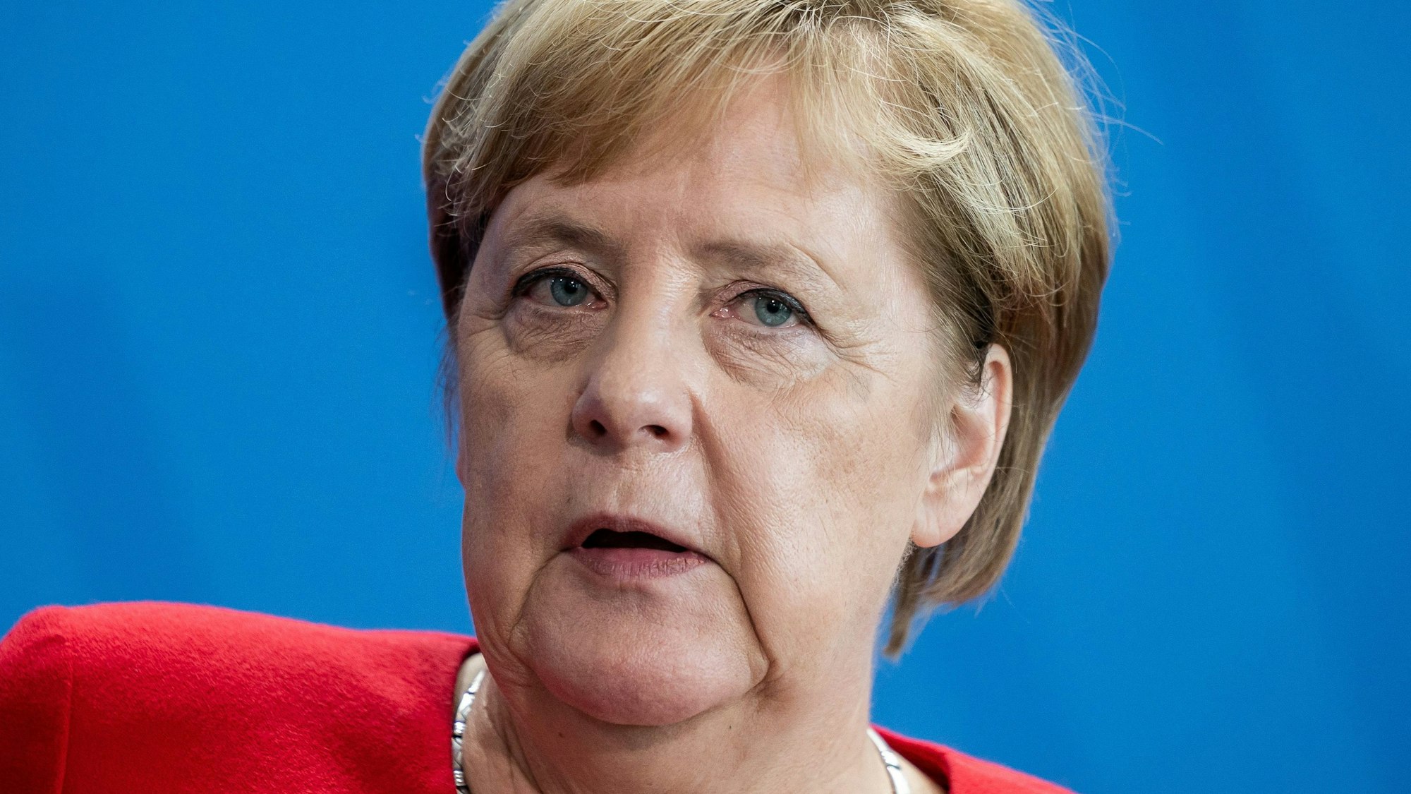 Ex-Bundeskanzlerin Angela Merkel blickt bei einer Pressekonferenz ins Publikum. Die CDU-Politikerin steht vor einer blauen Wand.