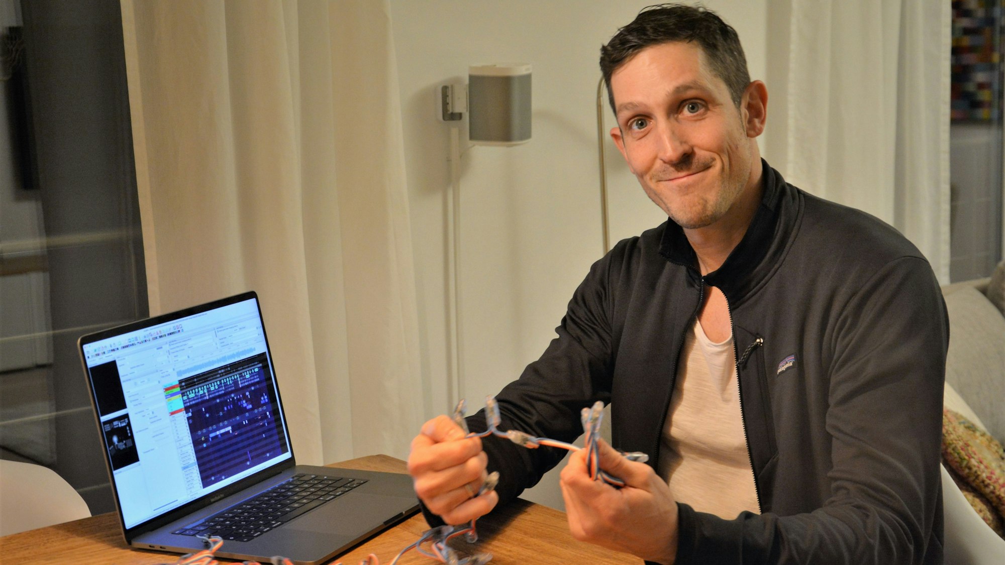 Simon Biela aus Köln-Müngersdorf in seiner Wohnung vor dem Laptop, an dem er die Lichtshow programmiert hat. In der Hand hält er eine der Lichterketten.