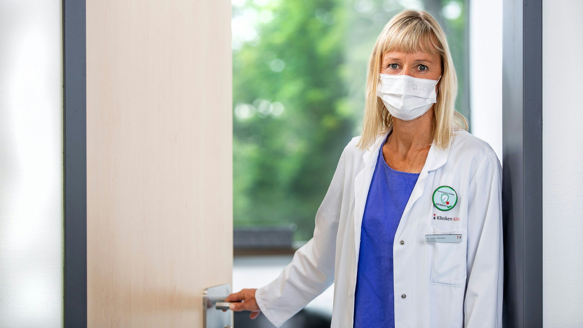 Iris Wimber steht im Kittel und mit Mundschutz an der Tür zu ihrem Büro in der Frauenklinik des Krankenhaus Holweide in Köln.