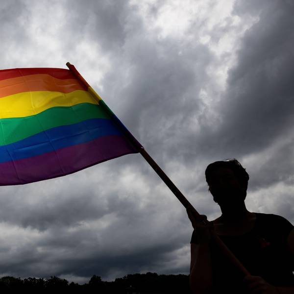 Eine Frau trägt die Regenbogenfahne bei einer Gedenkfeier. (Symbolbild)