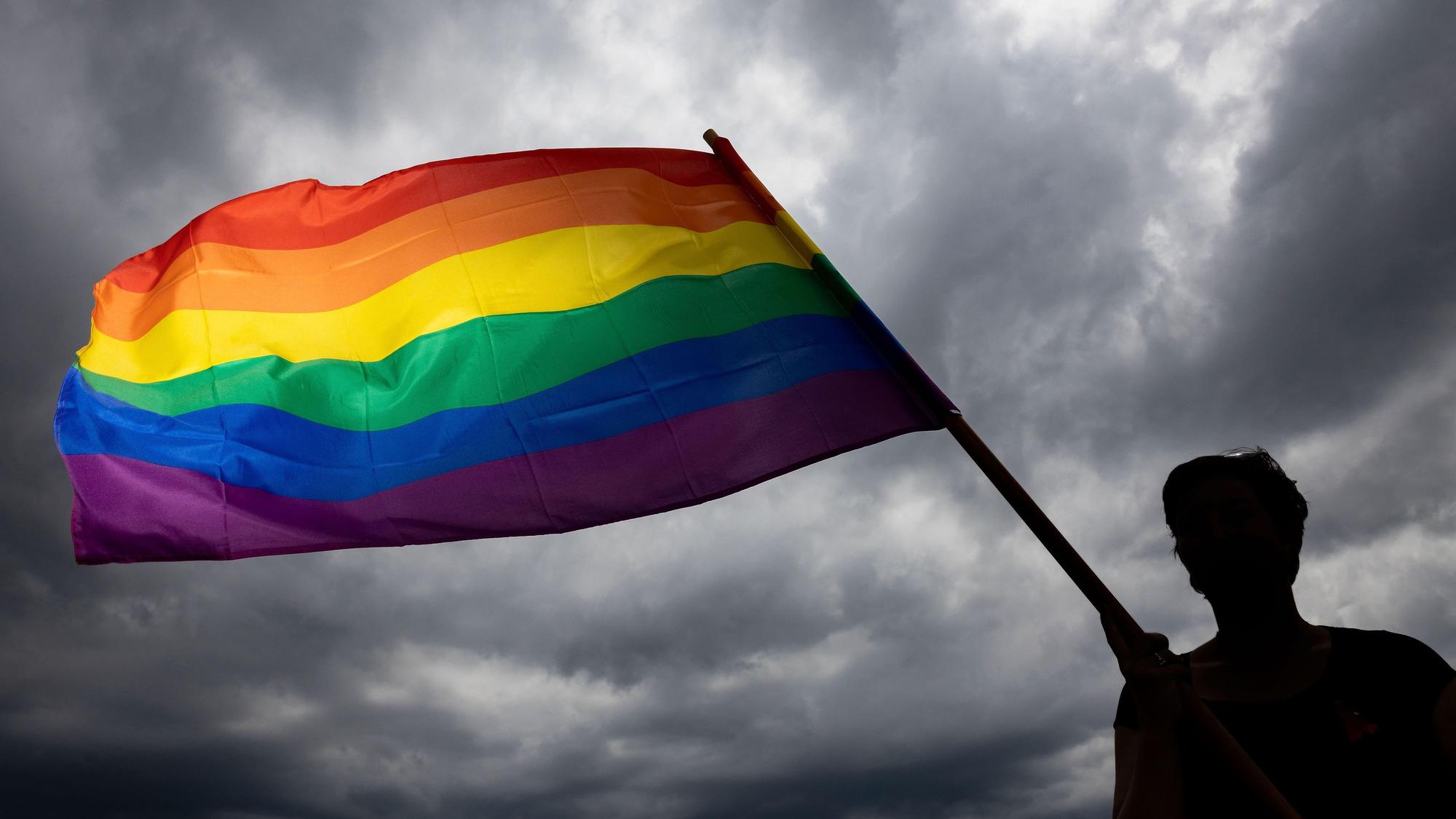 Eine Frau trägt die Regenbogenfahne bei einer Gedenkfeier. (Symbolbild)