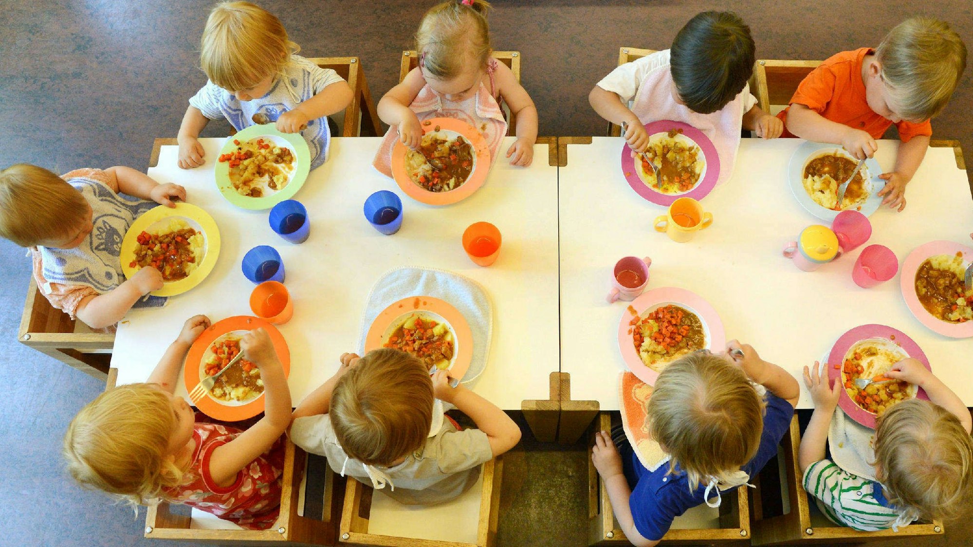 Kinder sitzen beim Mittagessen in einer Kindertageseinrichtung um einen Tisch.