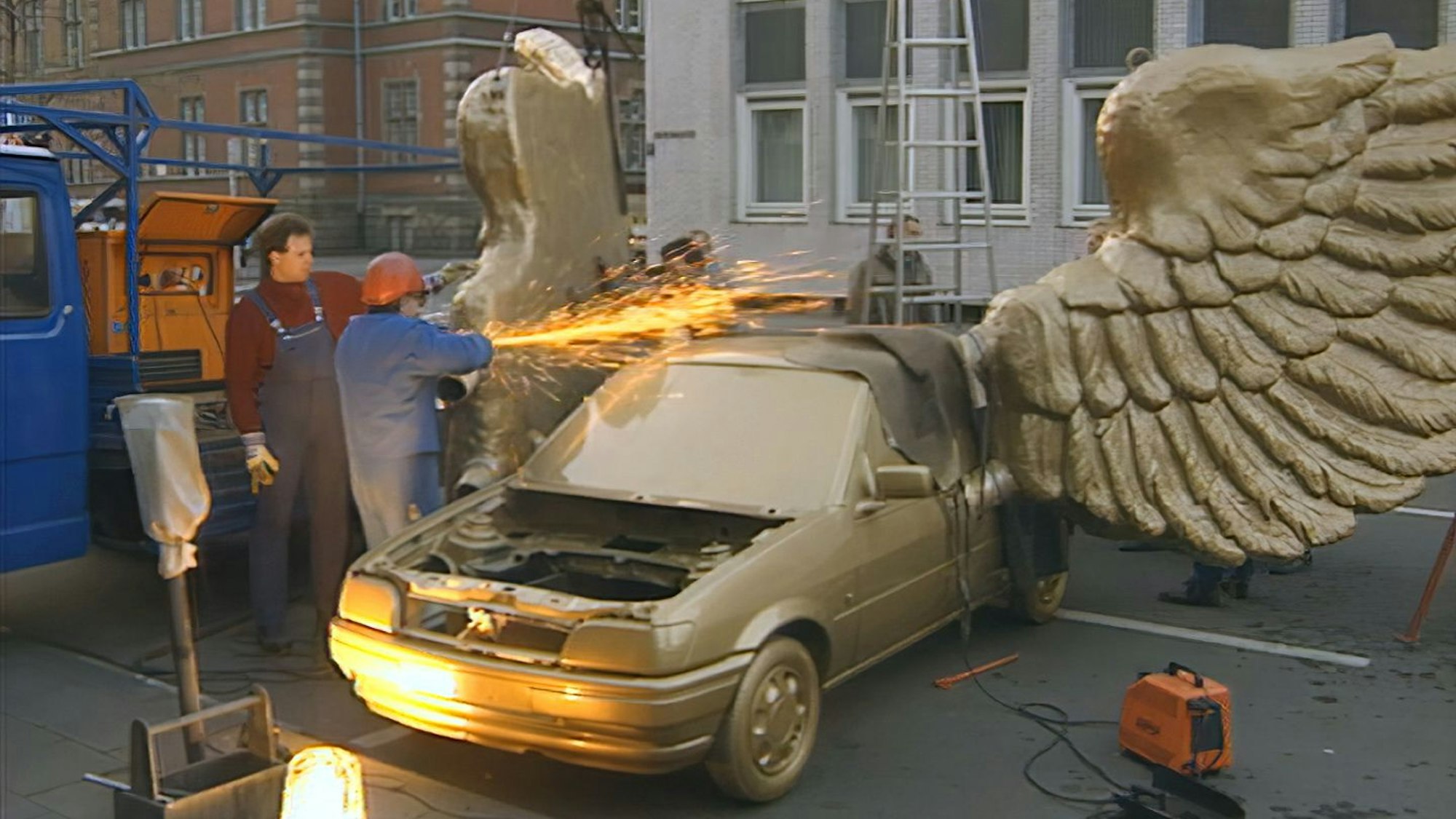 Ein Ford Fiesta, von Künstler HA Schult golden lackiert und mit Flügeln versehen, wird mit einer Trennscheibe bearbeitet.