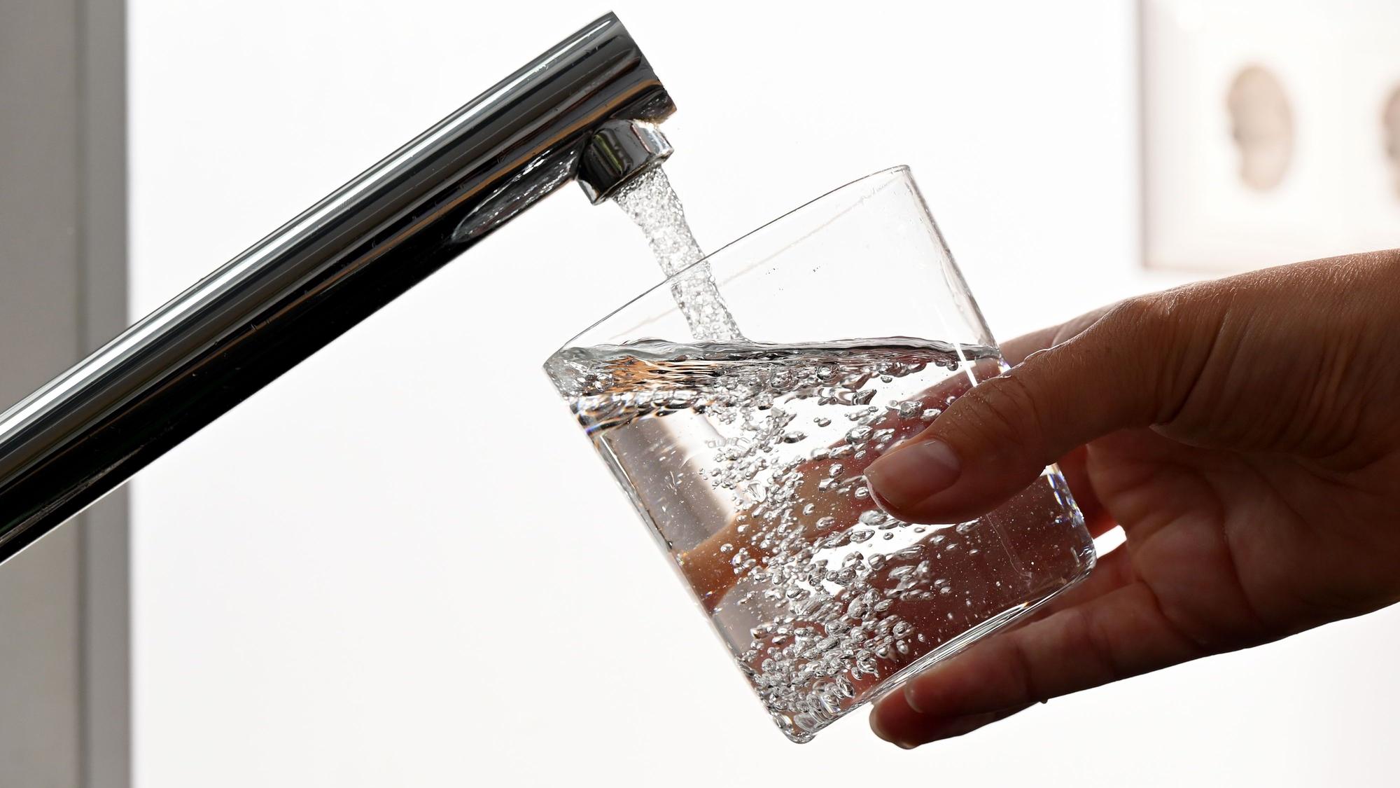 Eine Hand hält ein Wasserglas unter einen Wasserhahn.