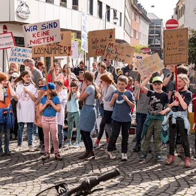 Schülerinnen und Schüler halten bei der Demo Plakate hoch, auf denen sie sich über das Verlosen von Plätzen beklagen.