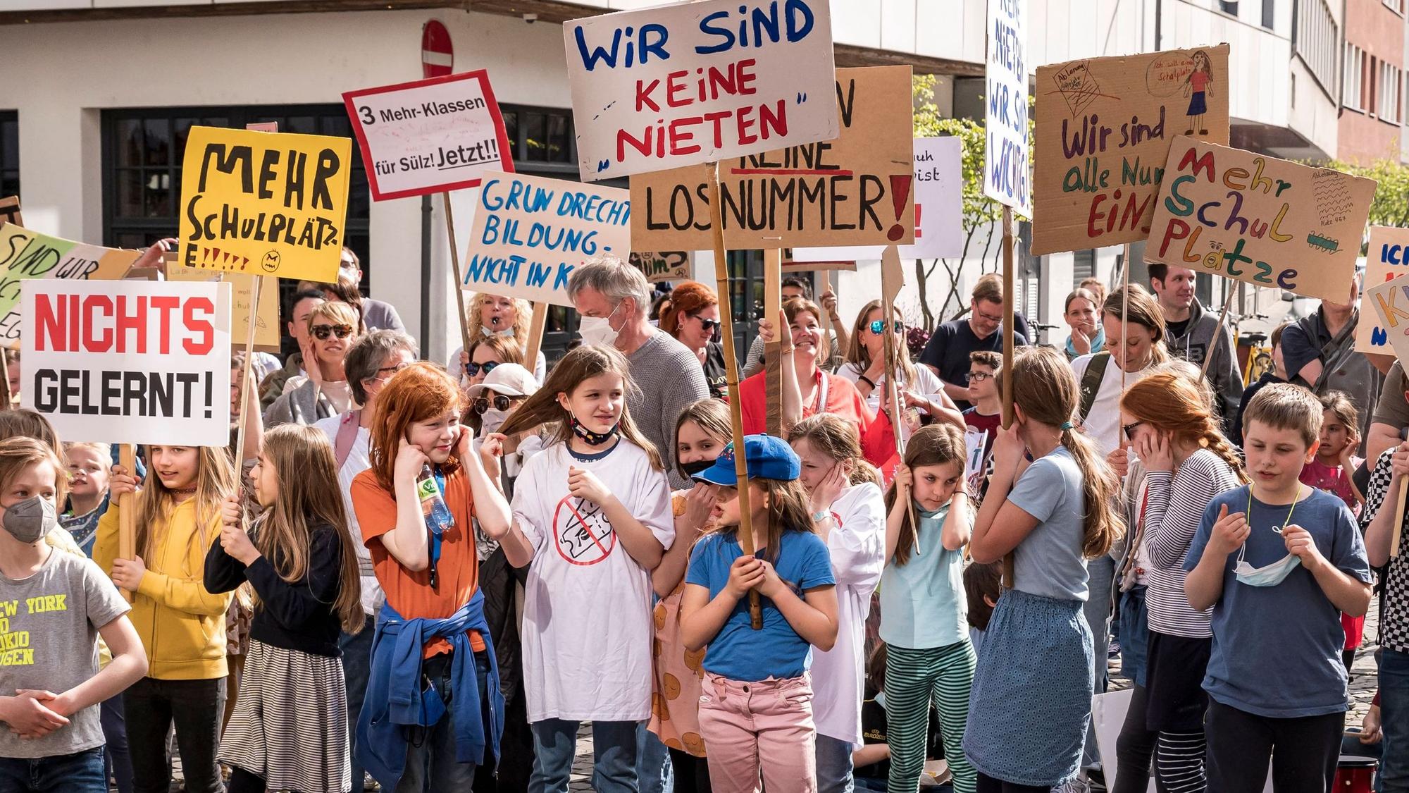 Schülerinnen und Schüler halten bei der Demo Plakate hoch, auf denen sie sich über das Verlosen von Plätzen beklagen.
