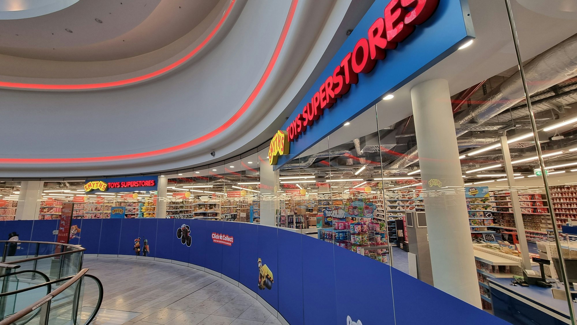 Außenansicht des Spielzeug-Geschäfts auf dem Obergeschoss der Rathaus-Galerie. Ein blau-gelb-roter Schriftzug „Smyths Toys Superstores“, gläserne Ladenverkleidung, dahinter viele Regale mit Spielzeug.