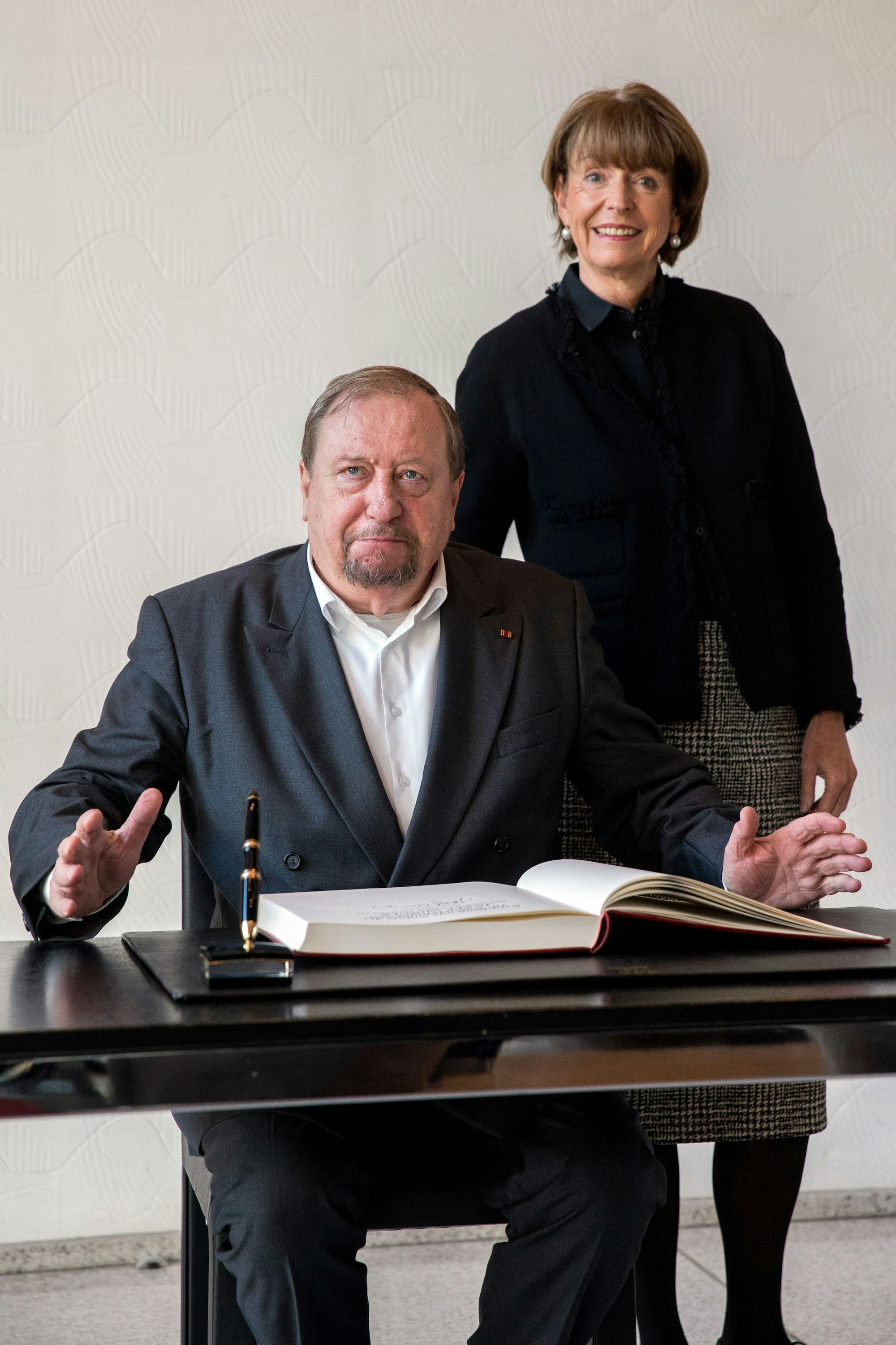 Josef Wirges beim Eintrag ins Gästebuch der Stadt Köln, hinter ihm steht Oberbürgermeisterin Henriette Reker und lächelt.
