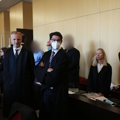 Der Hauptangeklagte (r) winkt zum Auftakt des Prozesses um eine Leverkusener Clan-Villa neben Anwälten im Gerichtssaal des Landgerichts. Angeklagt sind sieben Angehörige einer Großfamilie. Den Angeklagten werde vorgeworfen, zwischen 2014 und 2021 unberechtigt Sozialleistungen bezogen und Geldwäsche betrieben zu haben.