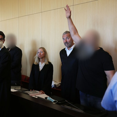 Der Hauptangeklagte (r) winkt zum Auftakt des Prozesses um eine Leverkusener Clan-Villa neben Anwälten im Gerichtssaal des Landgerichts. Angeklagt sind sieben Angehörige einer Großfamilie. Den Angeklagten werde vorgeworfen, zwischen 2014 und 2021 unberechtigt Sozialleistungen bezogen und Geldwäsche betrieben zu haben.