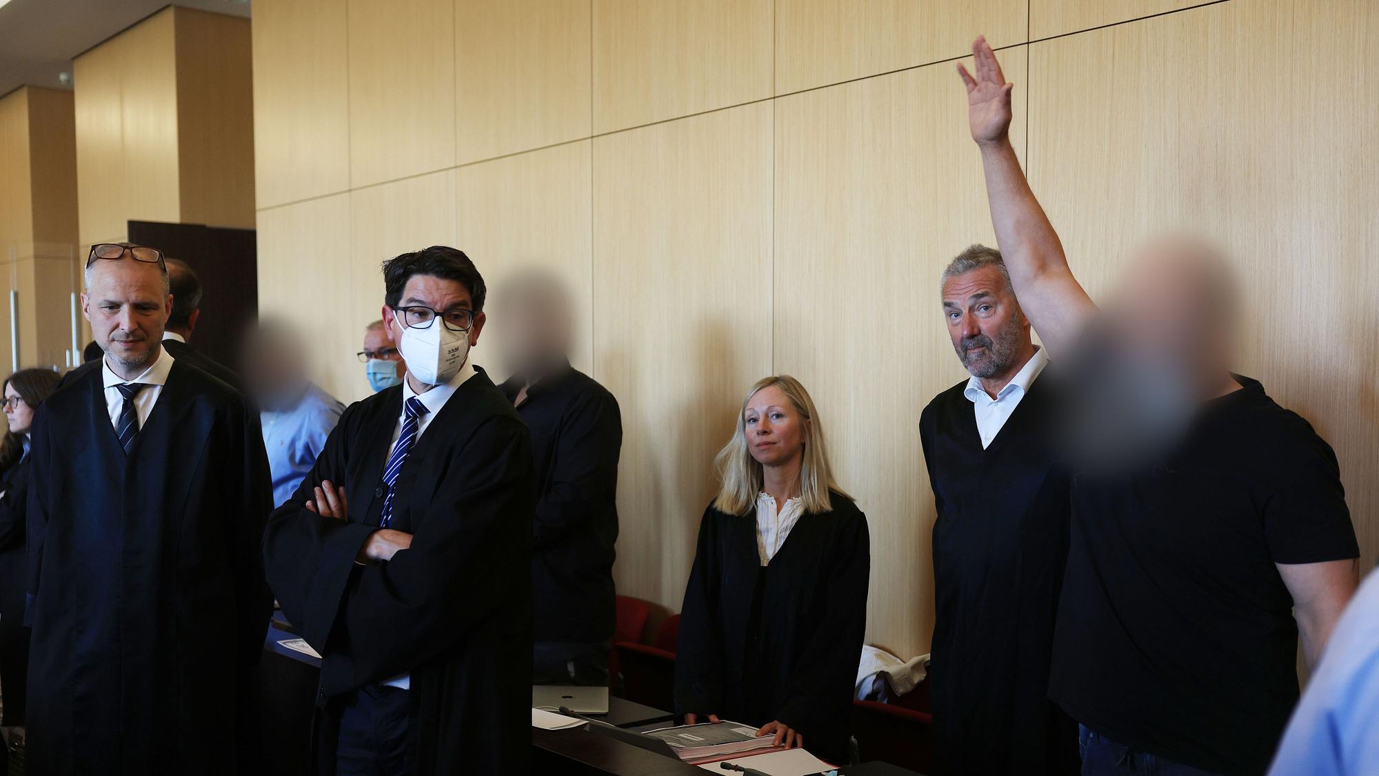 Der Hauptangeklagte (r) winkt zum Auftakt des Prozesses um eine Leverkusener Clan-Villa neben Anwälten im Gerichtssaal des Landgerichts. Angeklagt sind sieben Angehörige einer Großfamilie. Den Angeklagten werde vorgeworfen, zwischen 2014 und 2021 unberechtigt Sozialleistungen bezogen und Geldwäsche betrieben zu haben.
