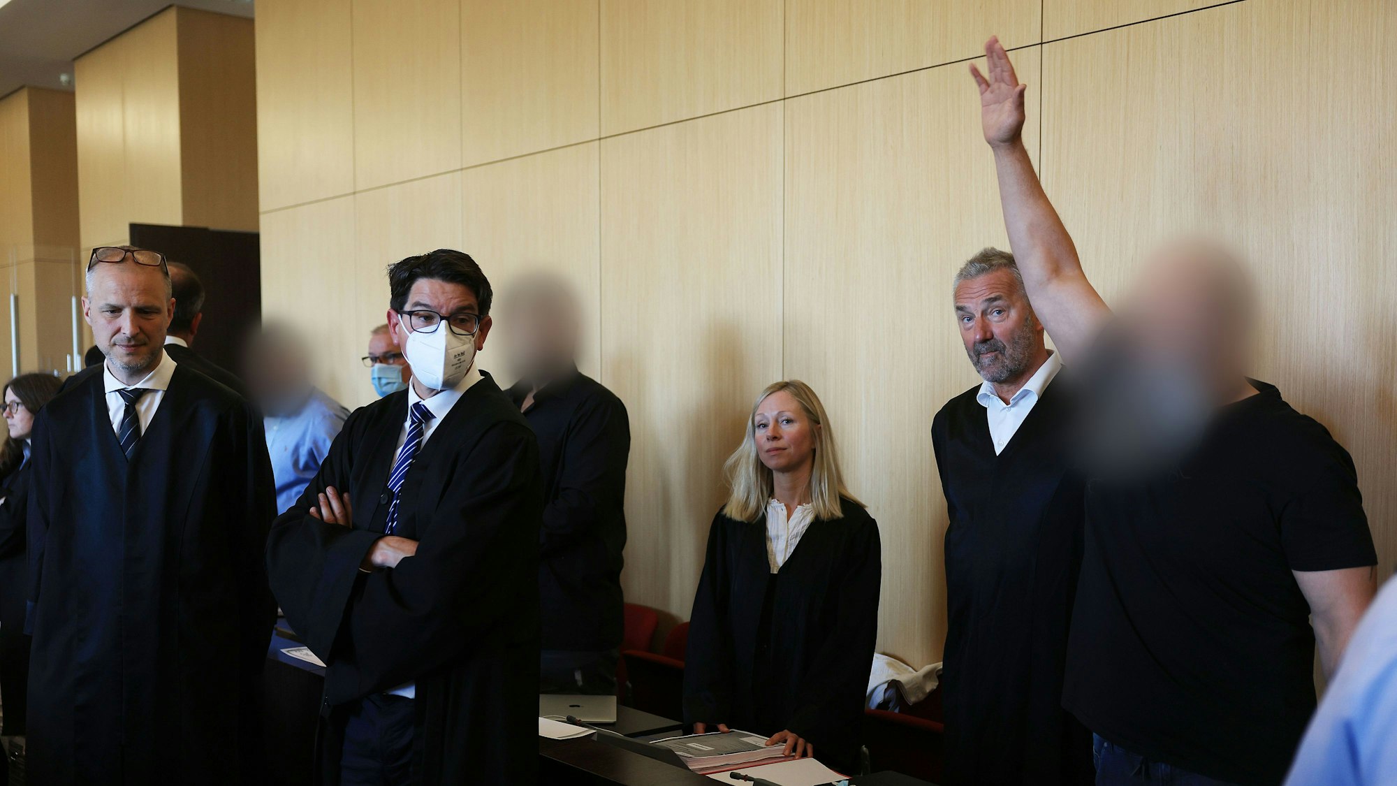 Der Hauptangeklagte (r) winkt zum Auftakt des Prozesses um eine Leverkusener Clan-Villa neben Anwälten im Gerichtssaal des Landgerichts. Angeklagt sind sieben Angehörige einer Großfamilie. Den Angeklagten werde vorgeworfen, zwischen 2014 und 2021 unberechtigt Sozialleistungen bezogen und Geldwäsche betrieben zu haben.