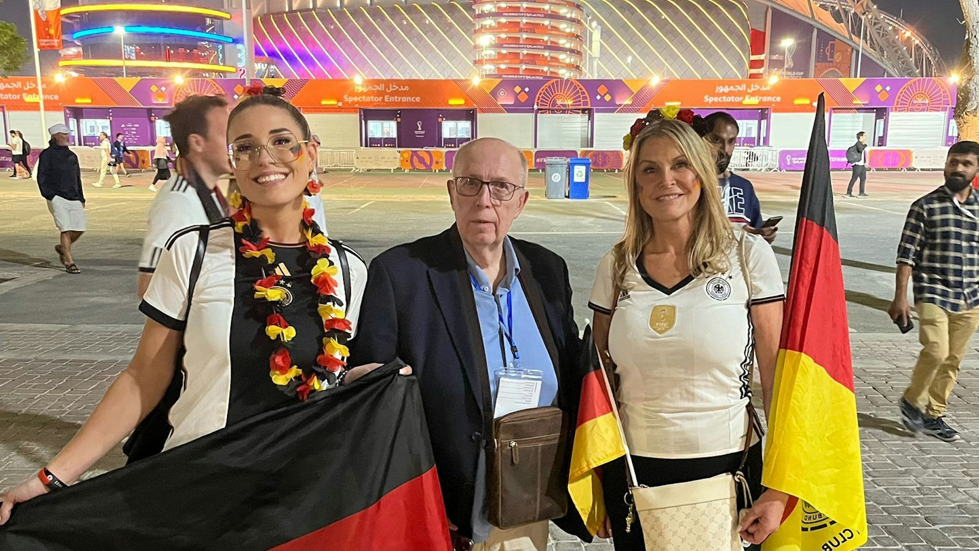 Reiner Calmund, der ein dunkelblaues Sakko trägt, lässt sich nach dem WM-Spiel zwischen Deutschland und Japan mit den deutschen Fans Elena (l.) und Elke Stegili vor dem Khalifa International Stadions in Al-Rayyan fotografieren.