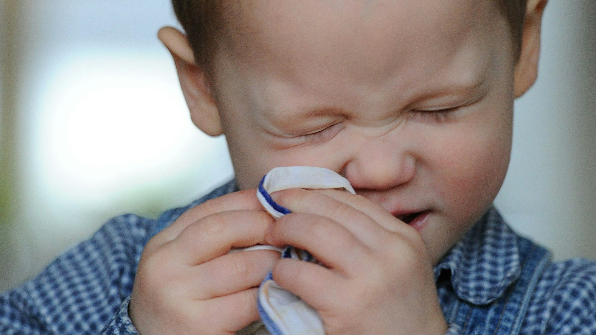 Ein Kleinkind niest in ein Stofftaschentuch (Symbolbild)