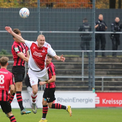 Ein Fußballer versucht, sich im Kopfball gegen drei Gegenspieler durchzusetzen.