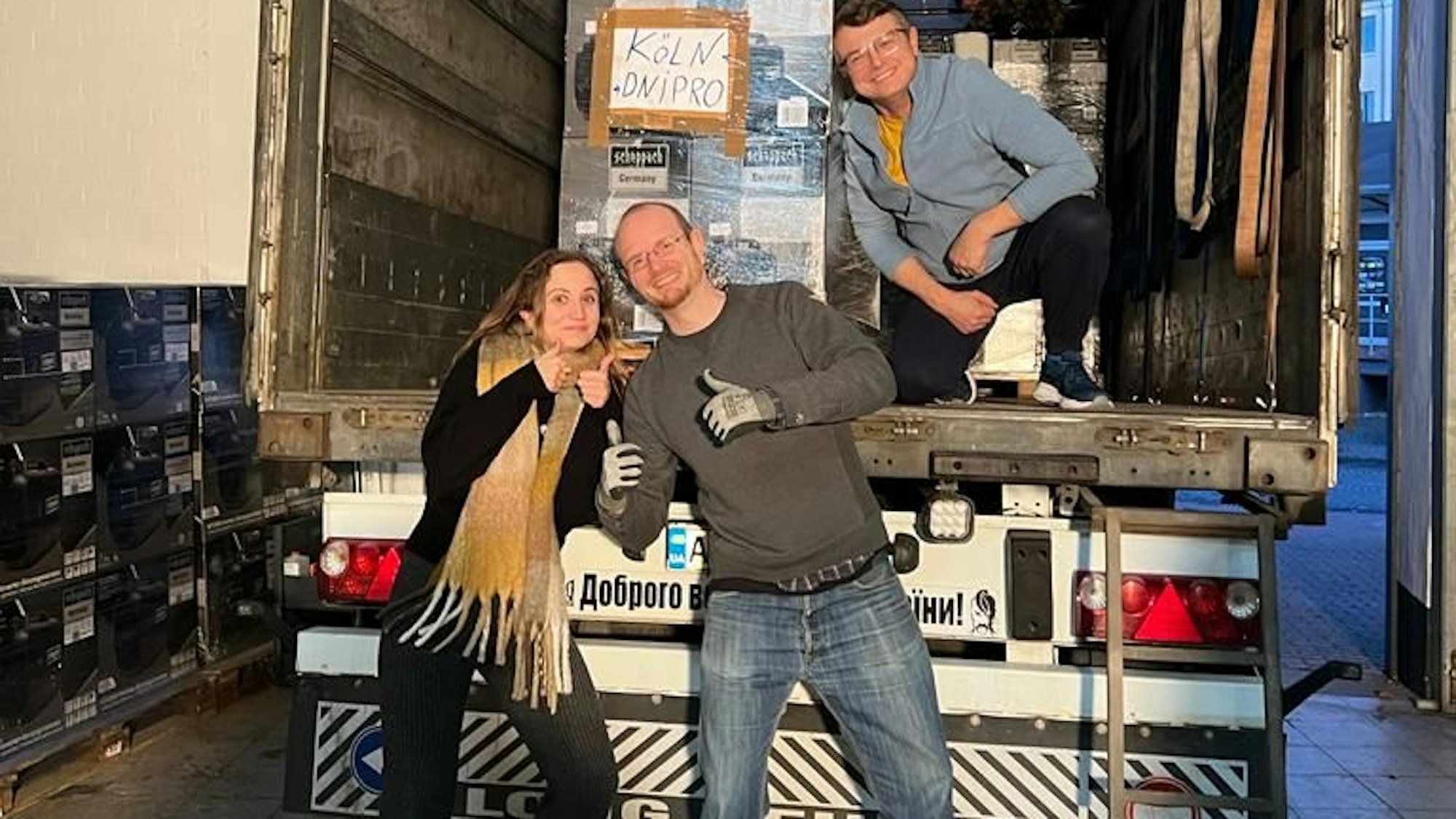 Viktoriiaanna Boiko, Jan Gutenschwager und Oleksandr Fadyeyev vom Blau-Gelben Kreuz stehn vor einem Lkw, den sie mit Matratzen, Generatoren und Kleidung beladen haben.