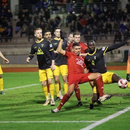 Im Strafraum des VfR Wipperfürth kommt VfR-Spieler Wael Majouj vor dem Aachener Spieler Exauce Andzouana an den Ball und klärt das Spielgerät ins Toraus. Im Hintergrund eine vollbesetzte Tribüne in der Bergisch Gladbacher Belkaw-Arena.