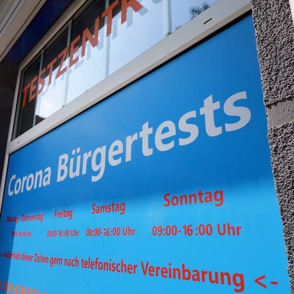 Ein Mann geht in ein Corona-Testzentrum. Ein Schild weist auf die Öffnungszeiten hin.