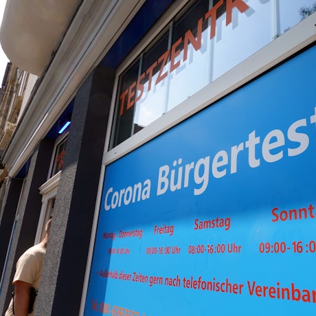 Ein Mann geht in ein Corona-Testzentrum. Ein Schild weist auf die Öffnungszeiten hin.