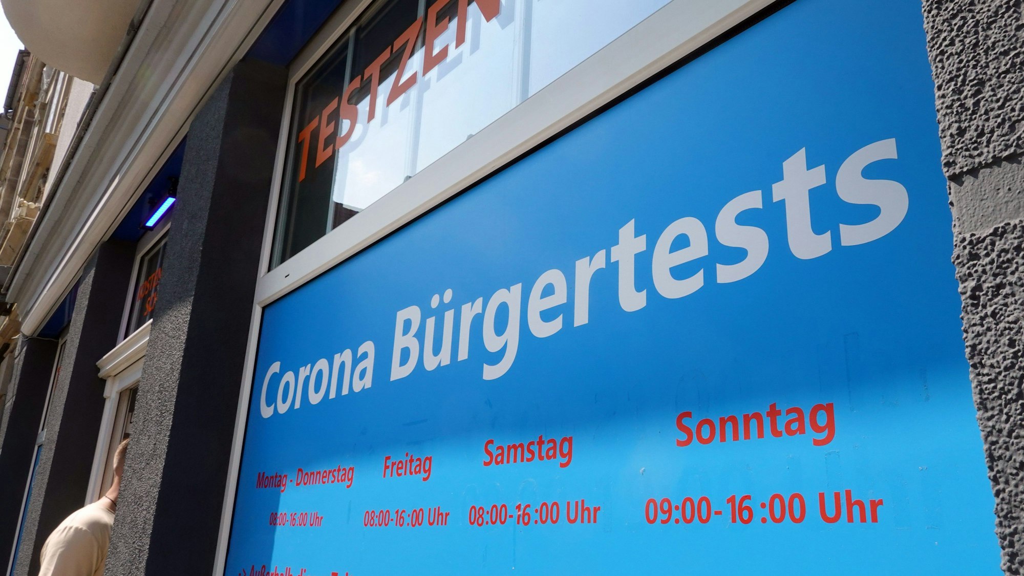 Ein Mann geht in ein Corona-Testzentrum. Ein Schild weist auf die Öffnungszeiten hin.