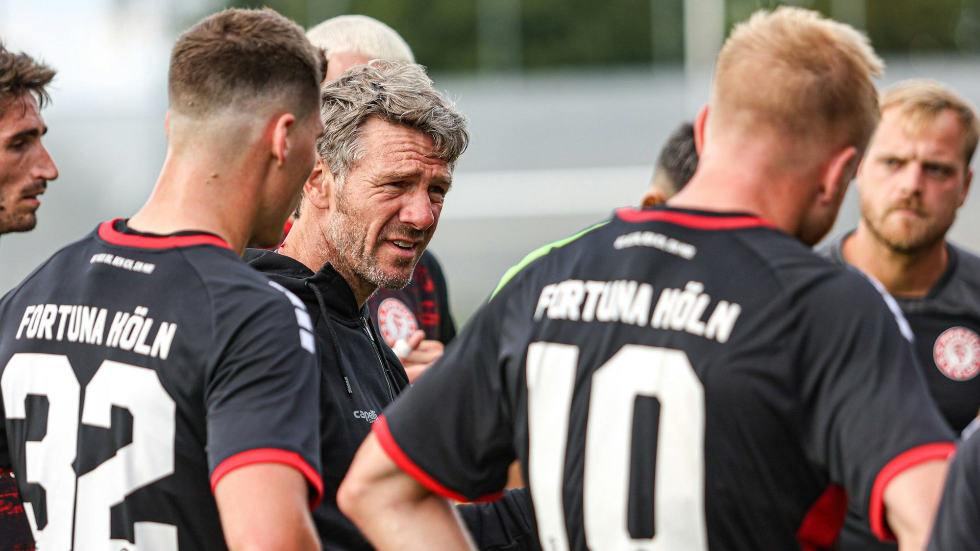 Ein Fußballtrainer steht bei einer Ansprache im Kreise seines Teams.