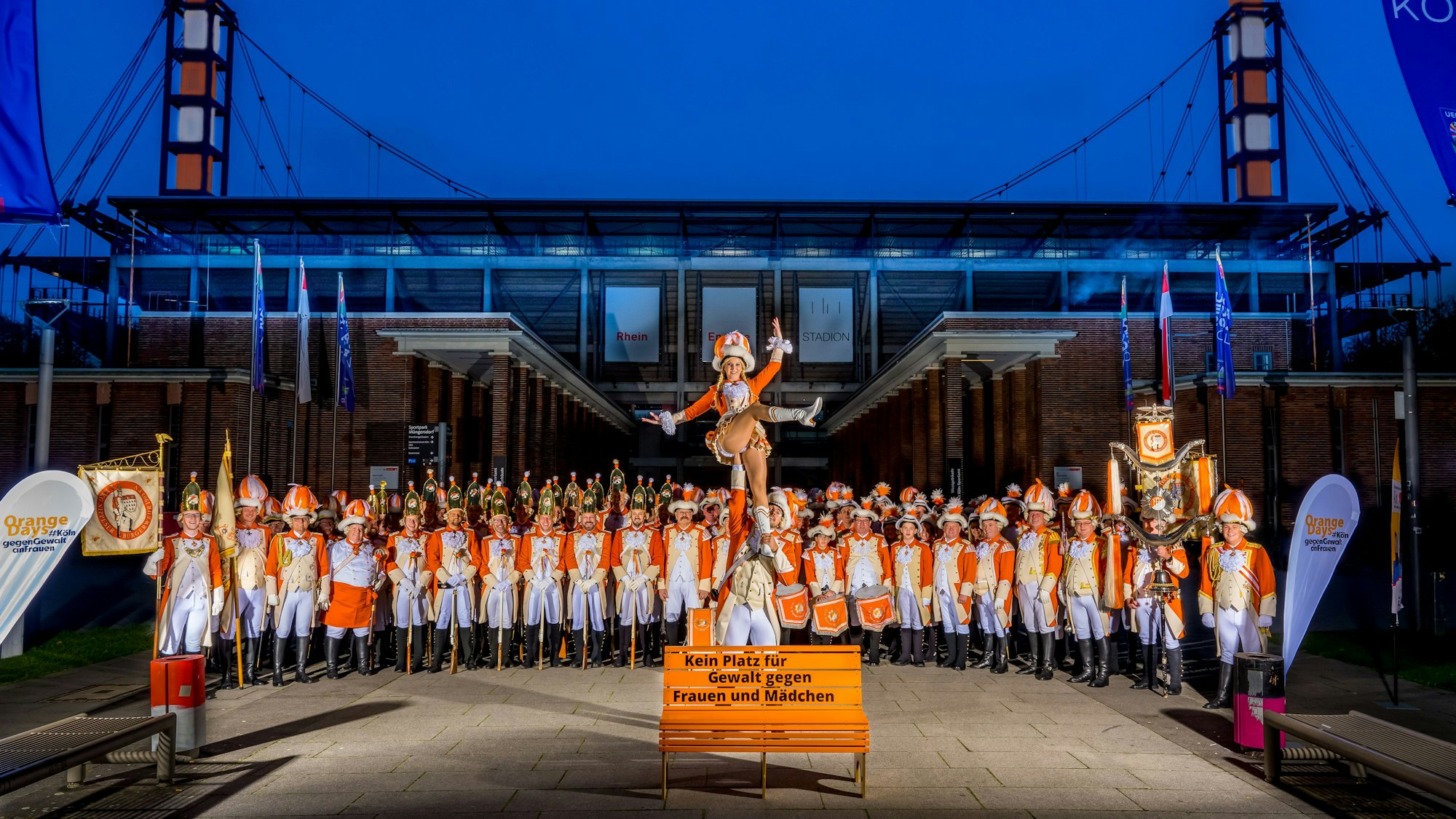 Die KKG Nippeser Bürgerwehr 1903 e.V. steht mit oranger Kleidung vor dem Rhein-Energie-Stadion und setzt damit ein Zeichen gegen Gewalt an Frauen.