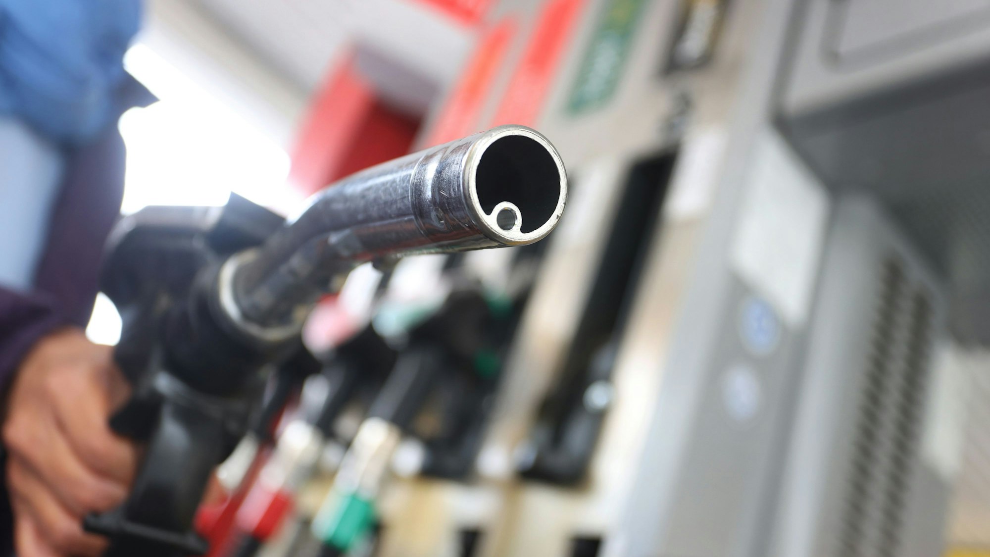 Eine Hand hält eine Zapfpistole auf einer Tankstelle.