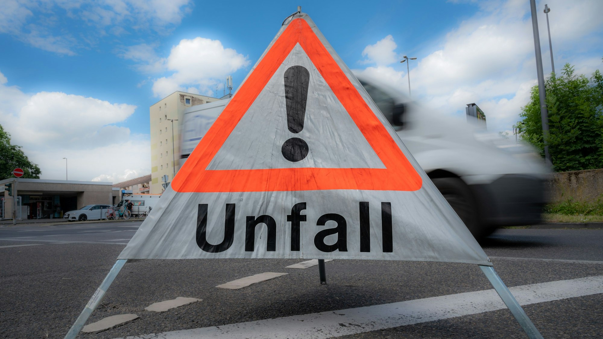Auf einer Straße steht ein mobiles „Unfall“-Schild. Dahinter ist ein verschwommener Van.