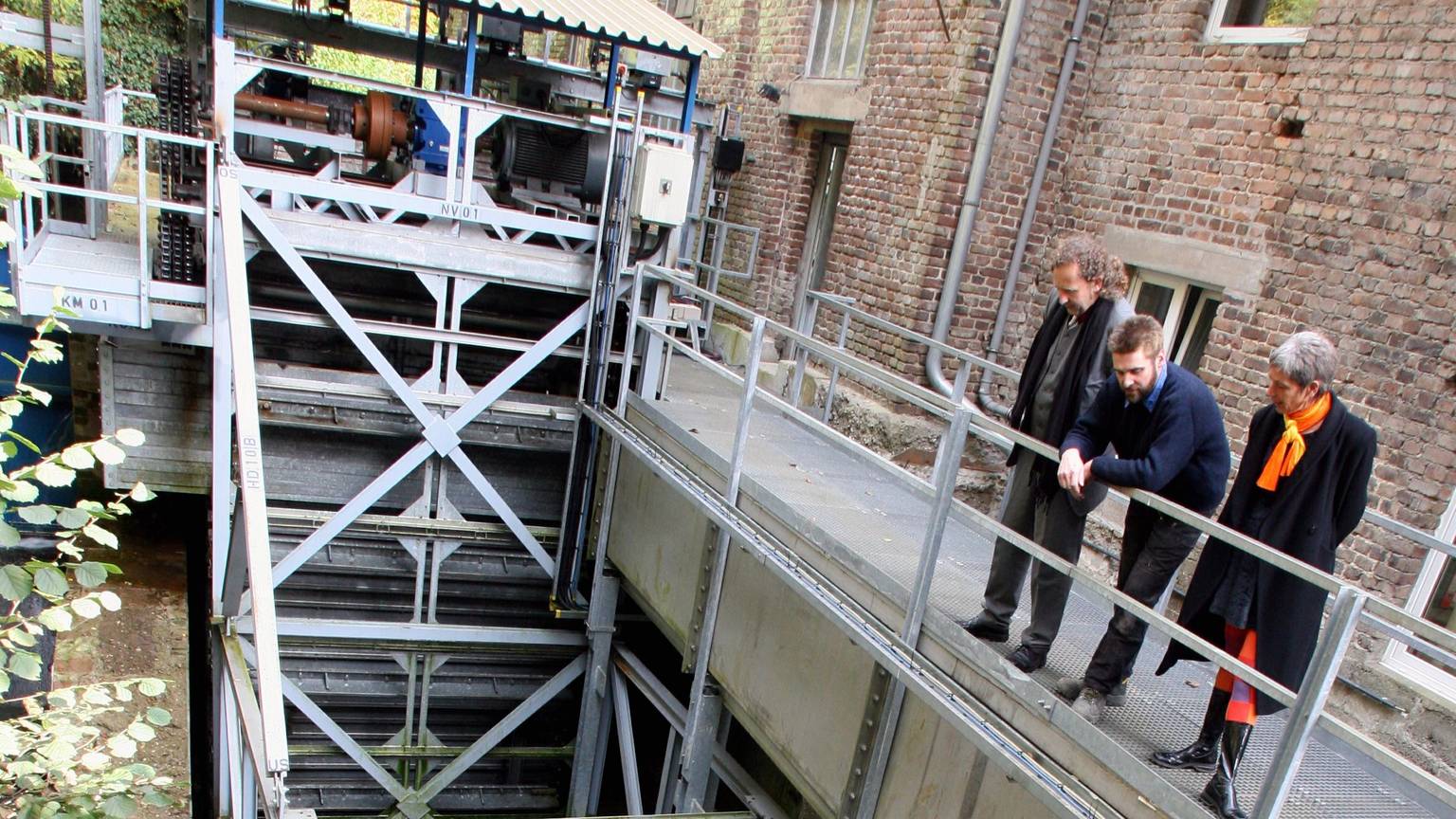 Drei Menschen schauen sich ein Wasserkraftwerk an.