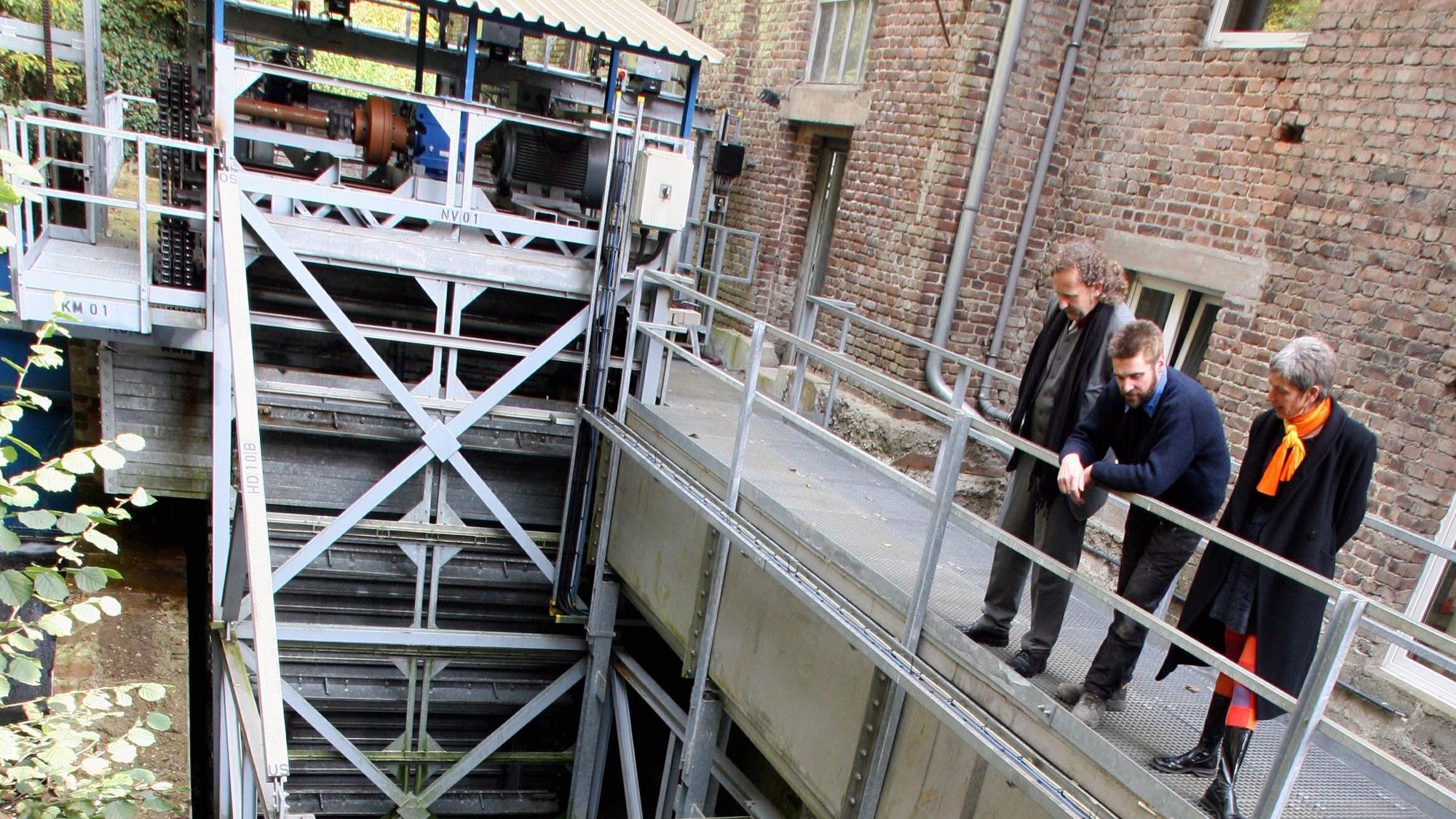 Drei Menschen schauen sich ein Wasserkraftwerk an.