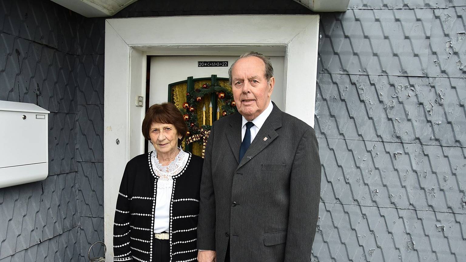 Zu sehen sind eine Frau und ein Mann, beide schick gekleidet, vor der Haustür ihres Wohnhauses in Bergneustadt.