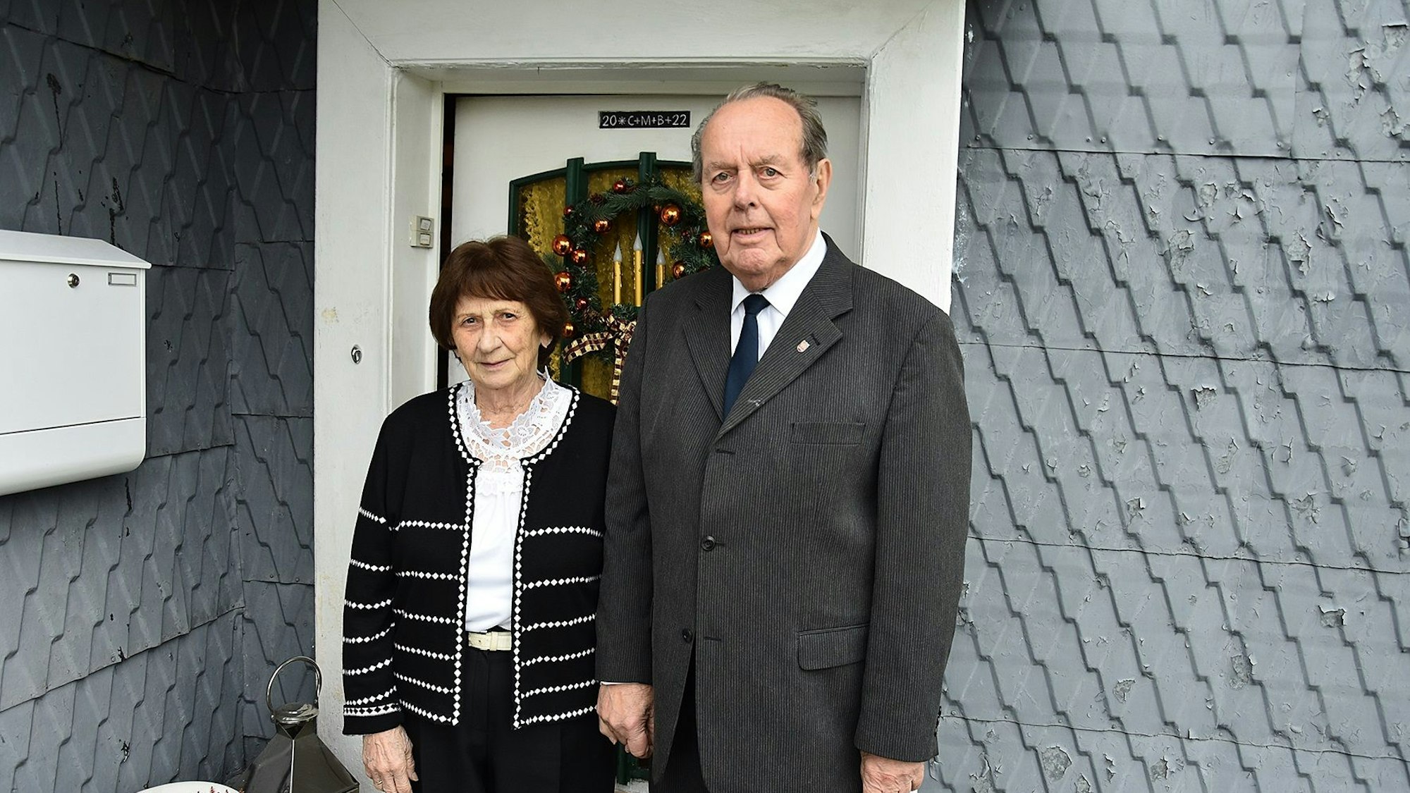 Zu sehen sind eine Frau und ein Mann, beide schick gekleidet, vor der Haustür ihres Wohnhauses in Bergneustadt.