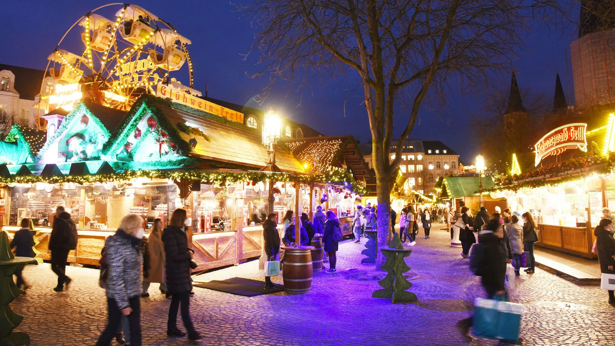 Die Weihnachtsmarktbuden leuchten im Dunkeln. Menschen gehen einzeln oder in kleinen Gruppen zwischen den Buden.