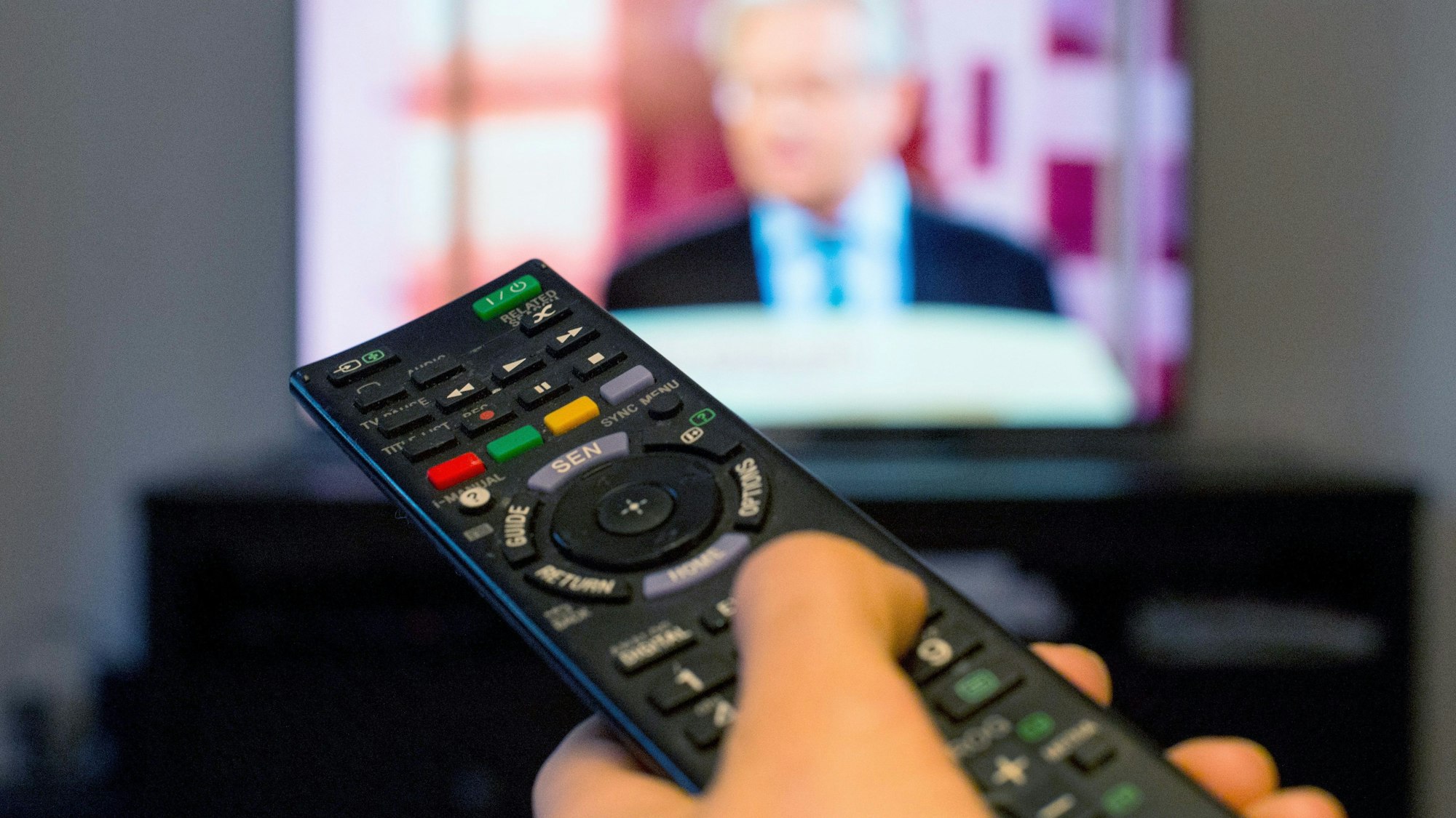 Eine Frau sitzt vor einem Fernseher und hält eine Fernbedienung in der Hand.