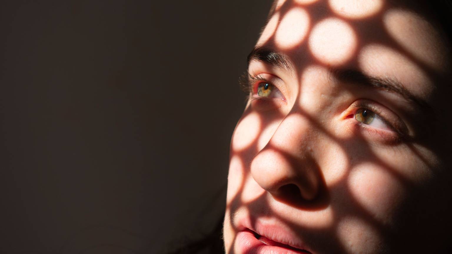 Porträt eines Mädchens, das traurig in ein Licht schaut, das runde Schatten auf sein Gesicht wirft.