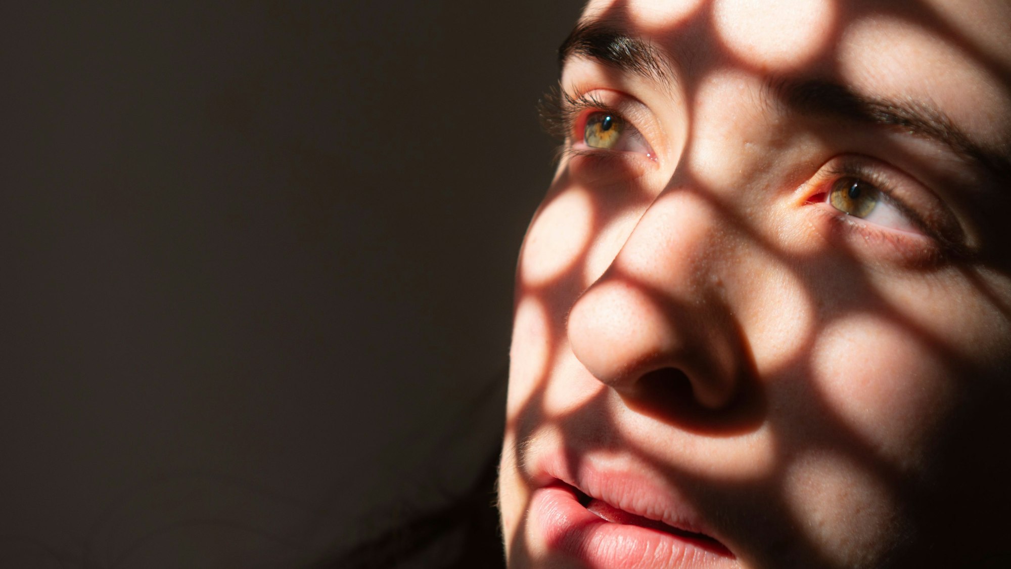 Porträt eines Mädchens, das traurig in ein Licht schaut, das runde Schatten auf sein Gesicht wirft.