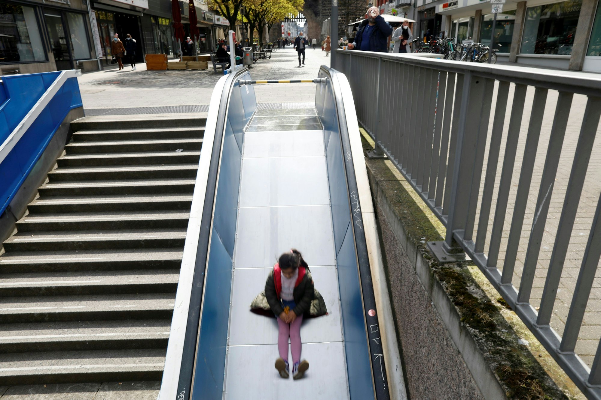 Das Bild zeigt ein Mädchen, das am Ebertplatz eine Rutsche auf einer kaputten Rolltreppe hinunter rutscht.
