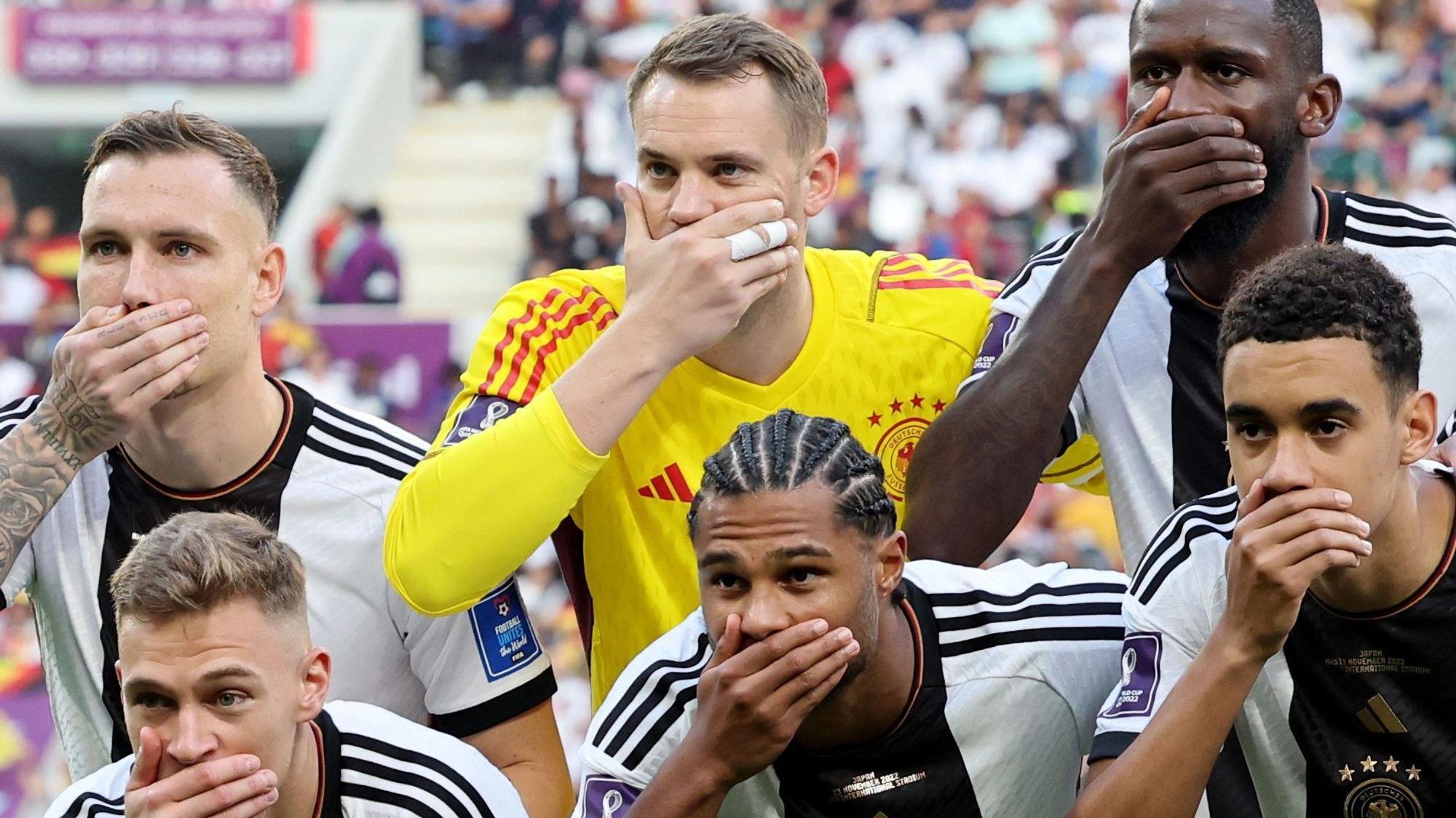 Die deutschen Fußball-Nationalspieler David Raum, Manuel Neuer, Antonio Rüdiger, Joshua Kimmich, Serge Gnabry und Jamal Musiala halten sich mit der jeweils rechten Hand den Mund zu. Das Foto zeigt einen Ausschnitt der gesamten Mannschaft vor dem WM-Vorrundenspiel gegen Japan.