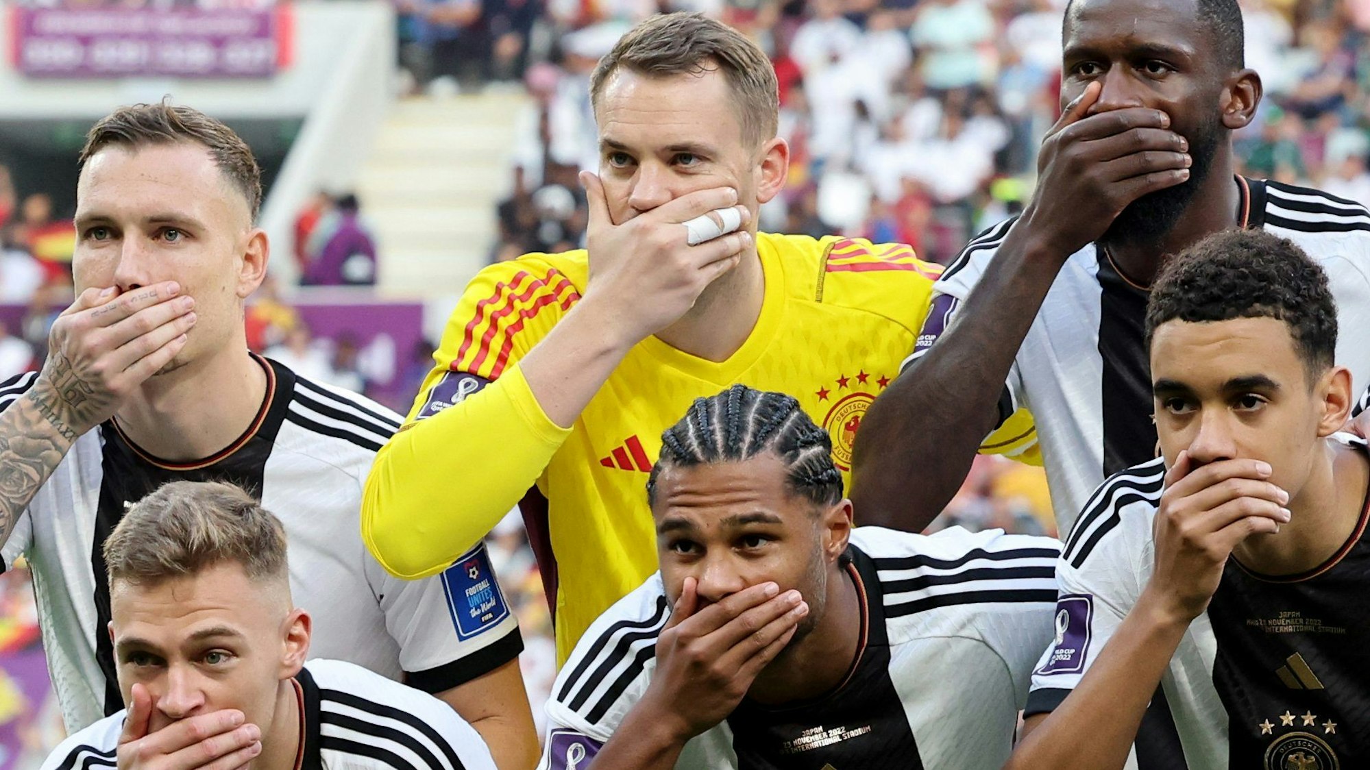 Die deutschen Fußball-Nationalspieler David Raum, Manuel Neuer, Antonio Rüdiger, Joshua Kimmich, Serge Gnabry und Jamal Musiala halten sich mit der jeweils rechten Hand den Mund zu. Das Foto zeigt einen Ausschnitt der gesamten Mannschaft vor dem WM-Vorrundenspiel gegen Japan.