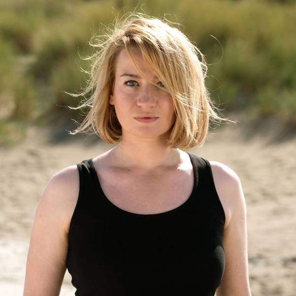 Nina Gummich in ihrer Rolle Alice Schwarzer, sie steht am Strand, hat ein schwarzes Top an