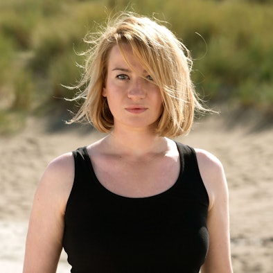 Nina Gummich in ihrer Rolle Alice Schwarzer, sie steht am Strand, hat ein schwarzes Top an