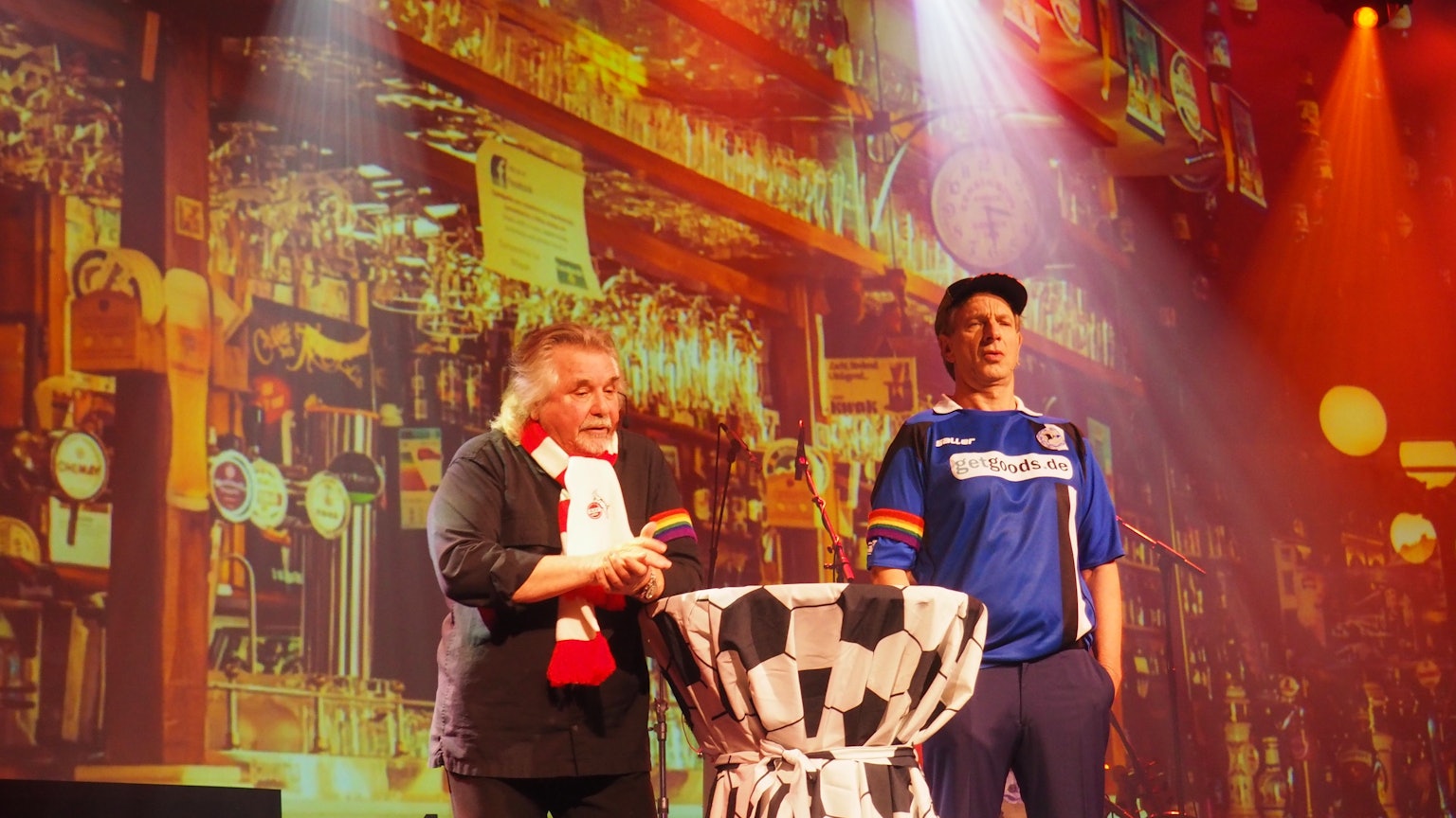 Tommy Engel und Ingolf Lück in Fußball-Trikot mit Regenbogen-Armbinde auf der Bühne des Weihnachtsengel.