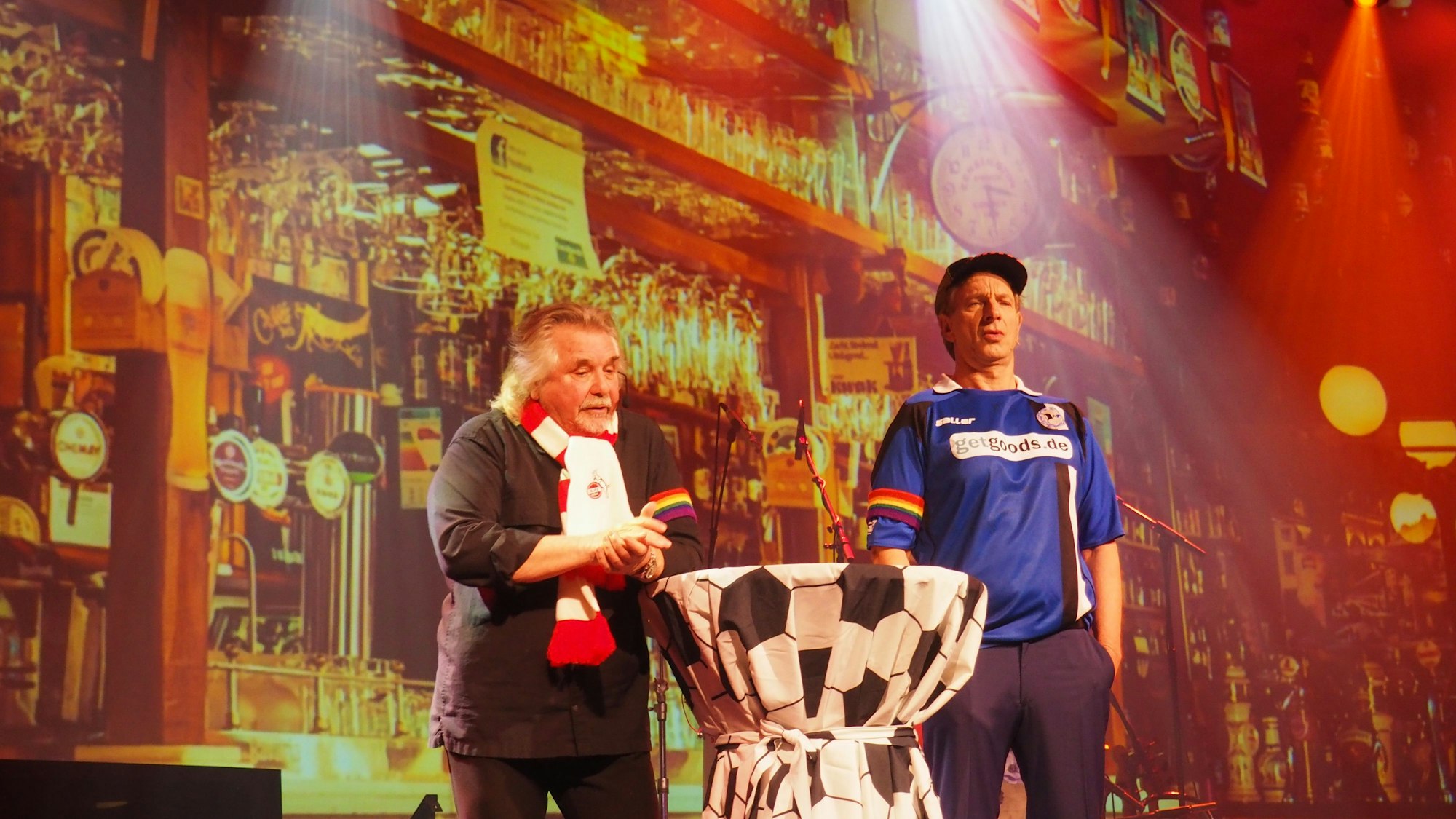 Tommy Engel und Ingolf Lück in Fußball-Trikot mit Regenbogen-Armbinde auf der Bühne des Weihnachtsengel.