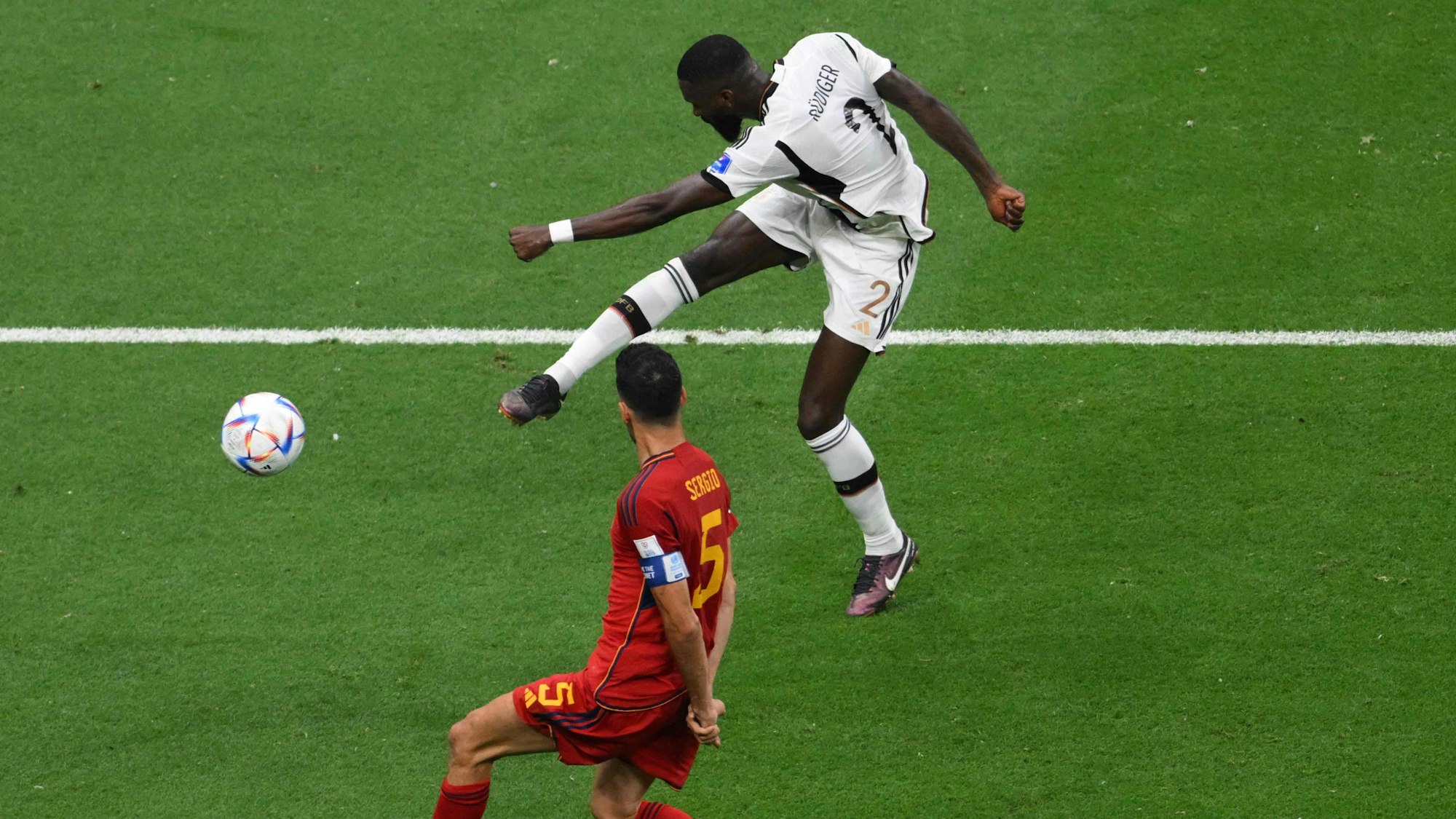 Antonio Rüdiger versucht im WM-Spiel gegen Spanien einen Fernschuss und macht dabei keine besonders elegante Figur. Spaniens Sergio Busquets versucht, den Schuss zu blocken.