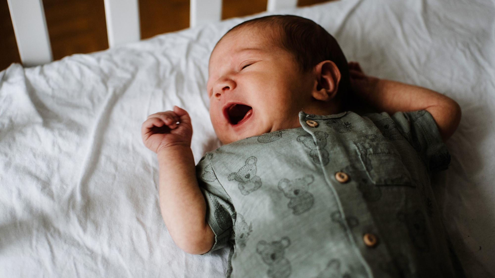 Ein Baby liegt im Bett und schreit.