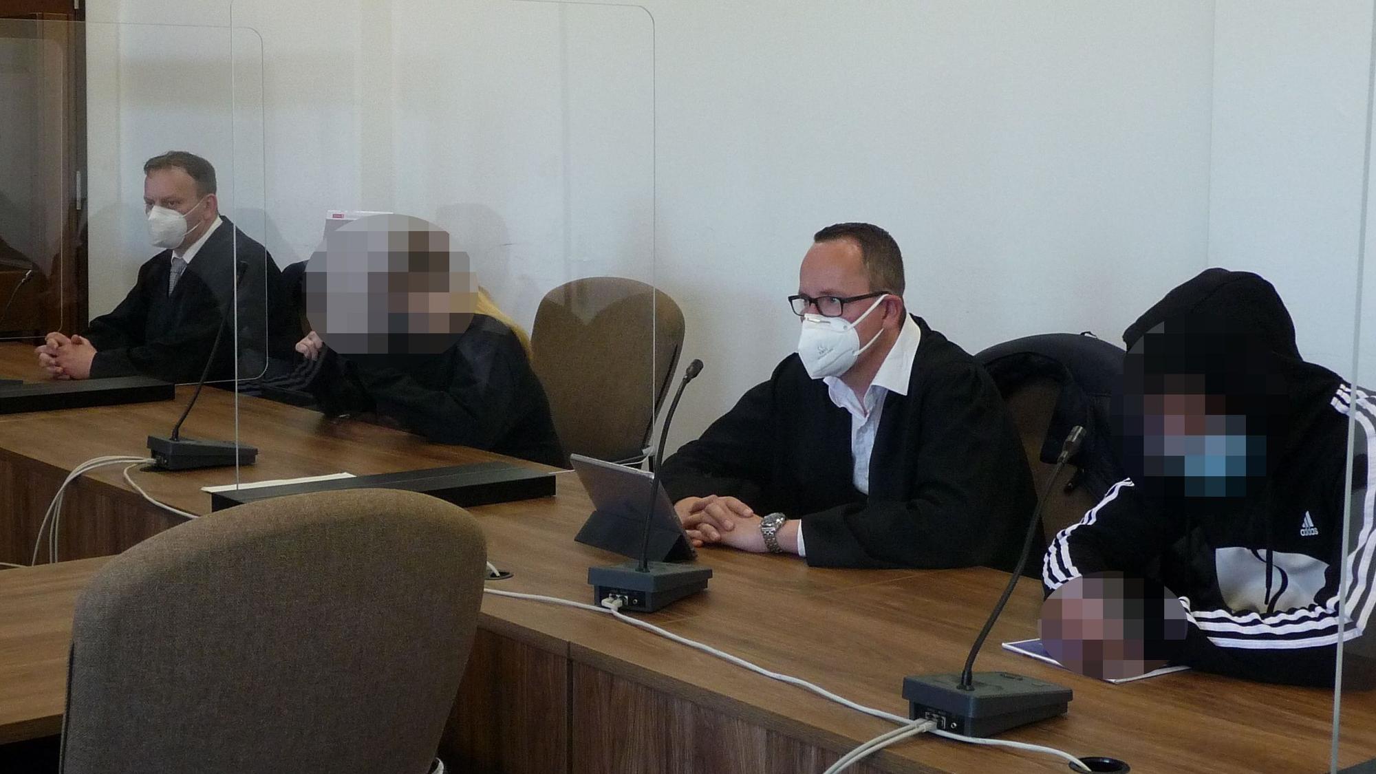 Eine Frau und ein Mann mit gepixelten Gesichtern sowie zwei Männer in Anwaltsrobe sitzen am Tisch einer Anklagebank im Kölner Landgericht.