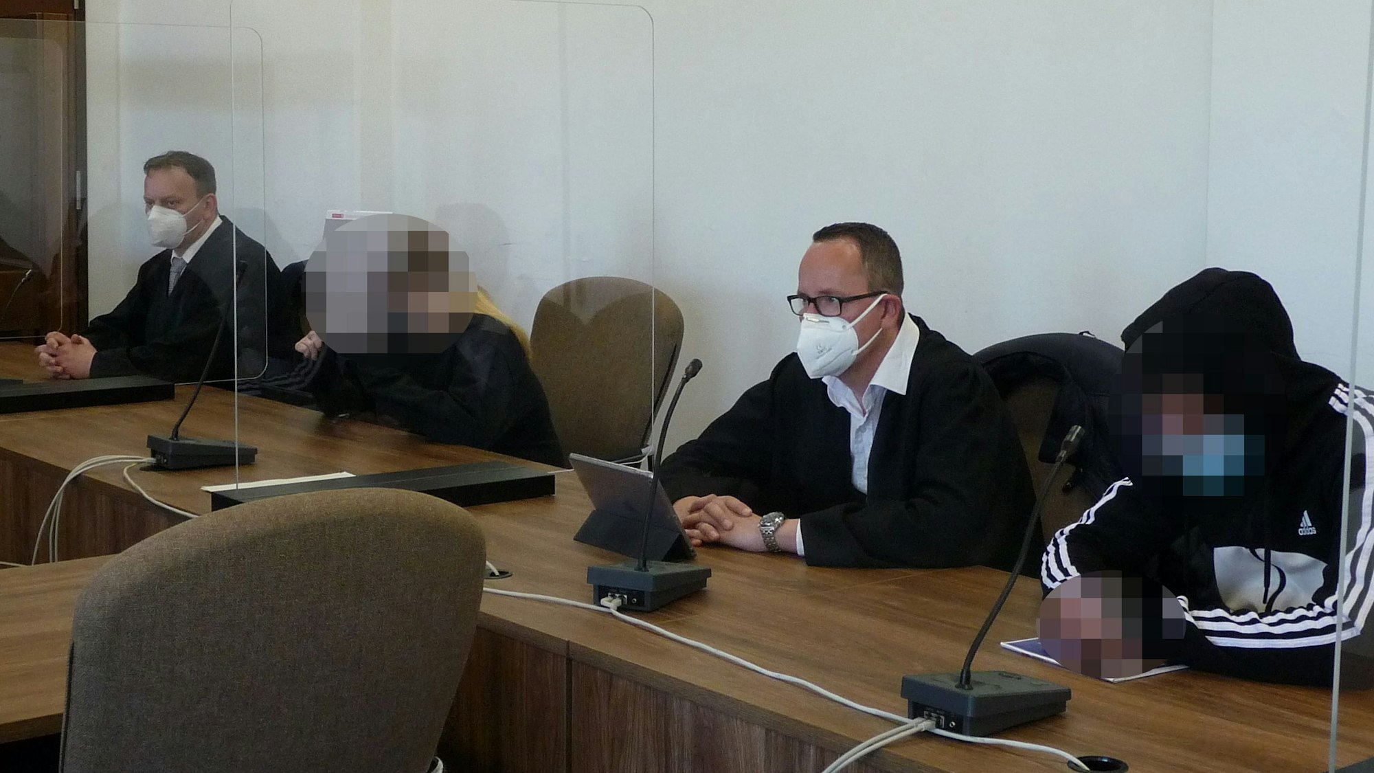 Eine Frau und ein Mann mit gepixelten Gesichtern sowie zwei Männer in Anwaltsrobe sitzen am Tisch einer Anklagebank im Kölner Landgericht.