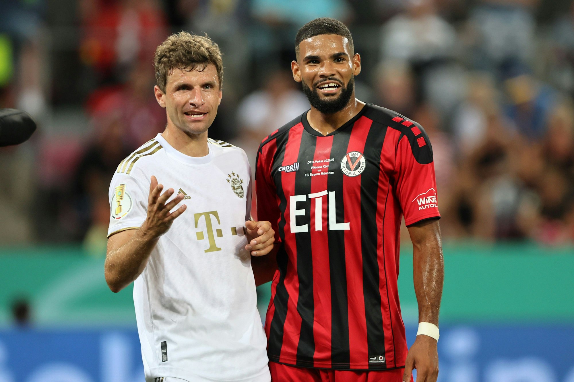 Zwei Fußballspieler stehen nebeneinander und lächeln.