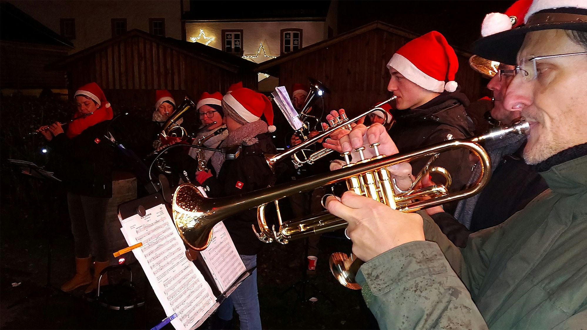 Die Mitglieder des Musikvereins Hecken haben rote Weihnachtsmützen aufgesetzt  und spielen auf dem Weihnachtsmarkt in Reifferscheid, im Vordergrund zwei Trompeter.